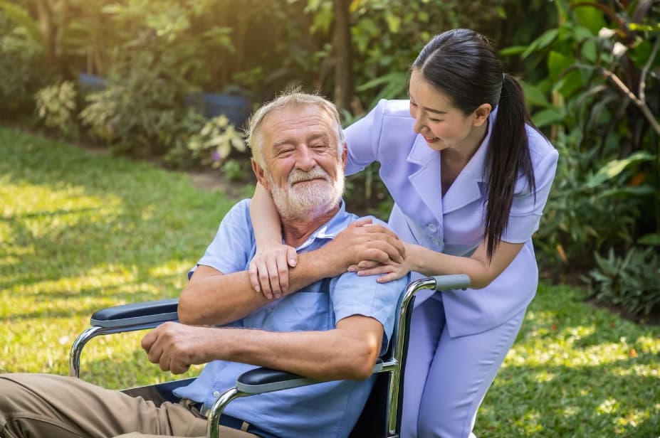 A caregiver sitting outdoors with an older adult in a wheelchair